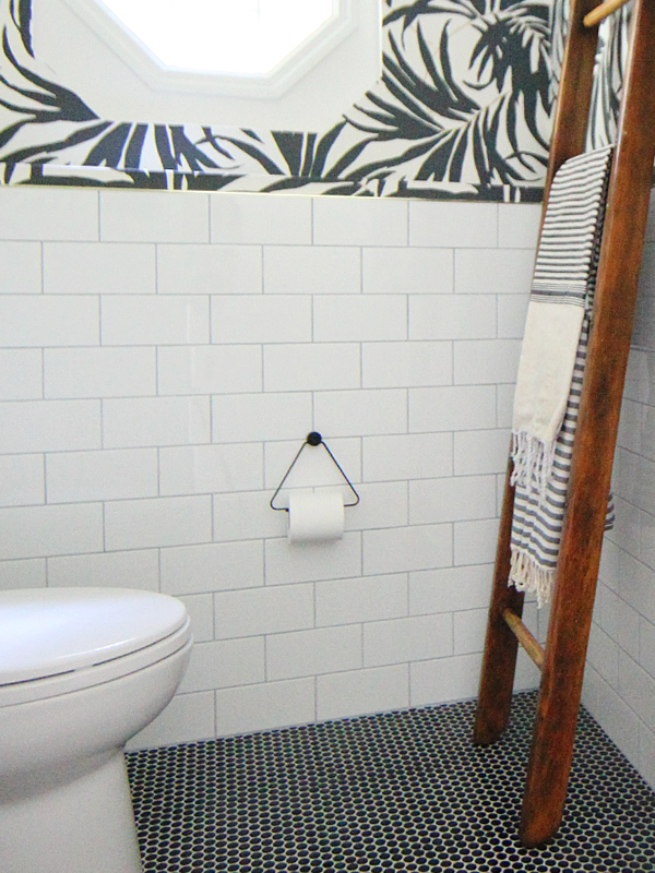 Basement Bathroom Makeover - White subway tile and black penny tile on the floor pairs with bold black and white palm leaf wallpaper.Turkish towels hang off a vintage wooden ladder — House Of Hipsters