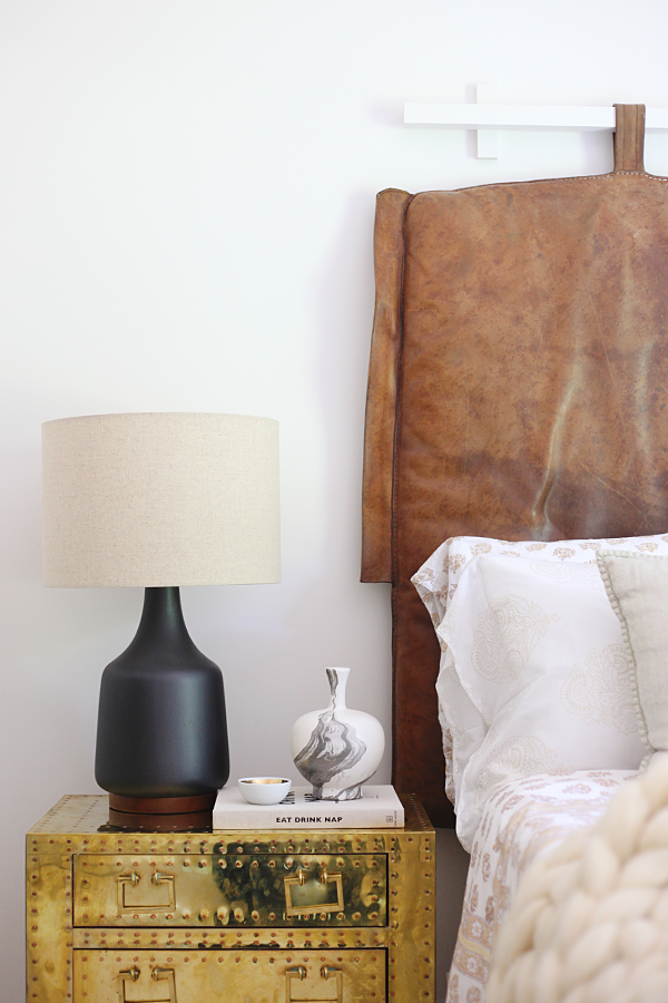 Royal Haeger Black and White Marbled Pottery Vase on brass Sarreid chest used as a nightstand. Vintage leather gym mat repurposed as a headboard. Everything But The House via House Of Hipsters