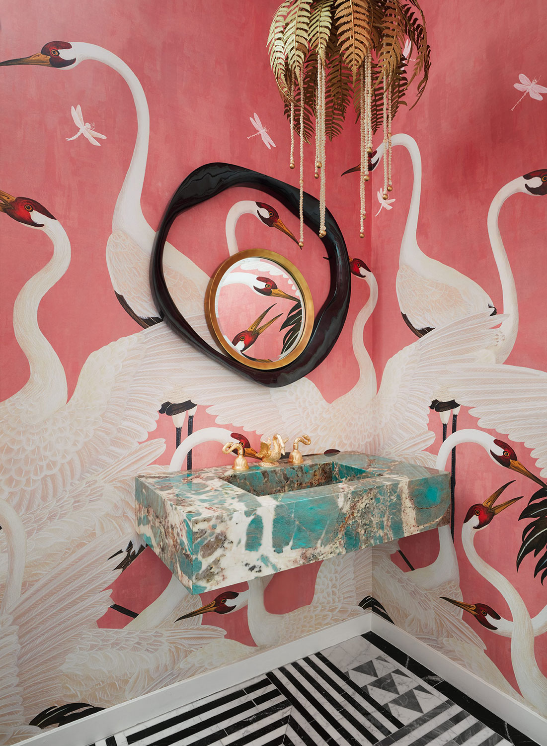 Gucci pink swan wallpaper adorned bathroom with solid green marble sink and brass palm leaf chandelier. 