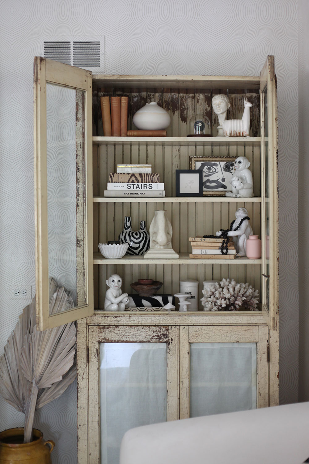 Shelf styling Antique chippy cabinet filled with vintage statues and books.